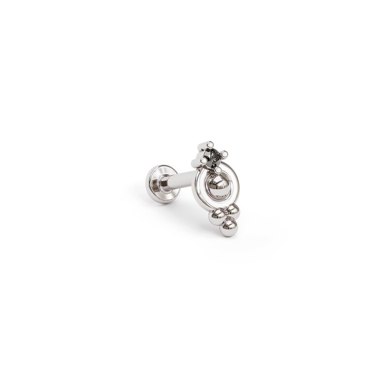 May include: Silver body jewelry with a black gemstone and a circle design with dangling beads.