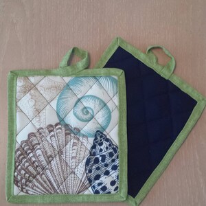 May include: Two quilted pot holders. One is green with a seashell pattern and the other is solid navy blue.