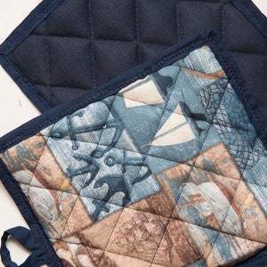 May include: Two quilted pot holders. One is navy blue with a quilted pattern. The other is a patchwork design with blue, brown, and white nautical themed patterns.
