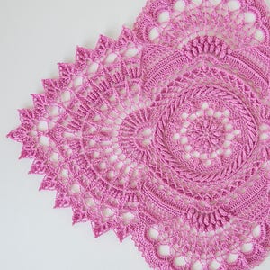May include: A pink crocheted doily with a circular design and intricate details.
