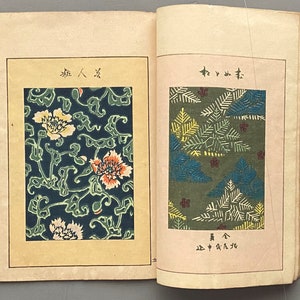 Op de afbeelding: Twee pagina's uit een vintage Japans boek met stoffenpatronen. De linkerpagina toont een bloemenpatroon met witte, gele, oranje en groene bloemen op een donkerblauwe achtergrond. De rechterpagina toont een groene achtergrond met een patroon van gestileerde dennennaalden in tinten groen, geel en blauw.
