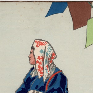 May include: A woman wearing a blue robe with a white and red patterned headscarf. She is sitting in profile and looking to the right. The background is a light blue with a brown and blue flag hanging from a bamboo pole.