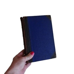 Puede incluir: Un libro de tapa dura azul con lomo marr&oacute;n.
