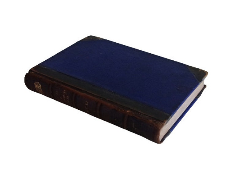 Puede incluir: Un libro antiguo de tapa dura con una cubierta azul oscuro y letras doradas en el lomo. El libro est&aacute; encuadernado en cuero marr&oacute;n y tiene un aspecto desgastado y envejecido.