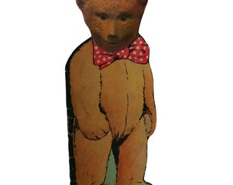Puede incluir: Un recorte de cartón plano troquelado de un oso de peluche marrón de pie. El oso tiene la cabeza de color marrón oscuro, el cuerpo de color tostado claro y lleva una pajarita roja brillante con lunares blancos. La ilustración tiene contornos negros.