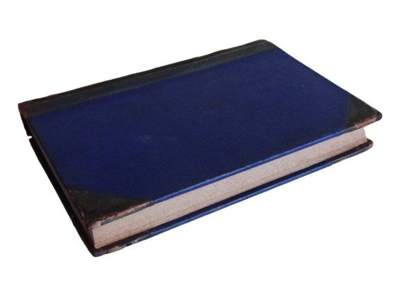 Puede incluir: Un libro de tapa dura azul con un aspecto desgastado y antiguo. El libro est&aacute; cerrado y acostado sobre un fondo blanco.