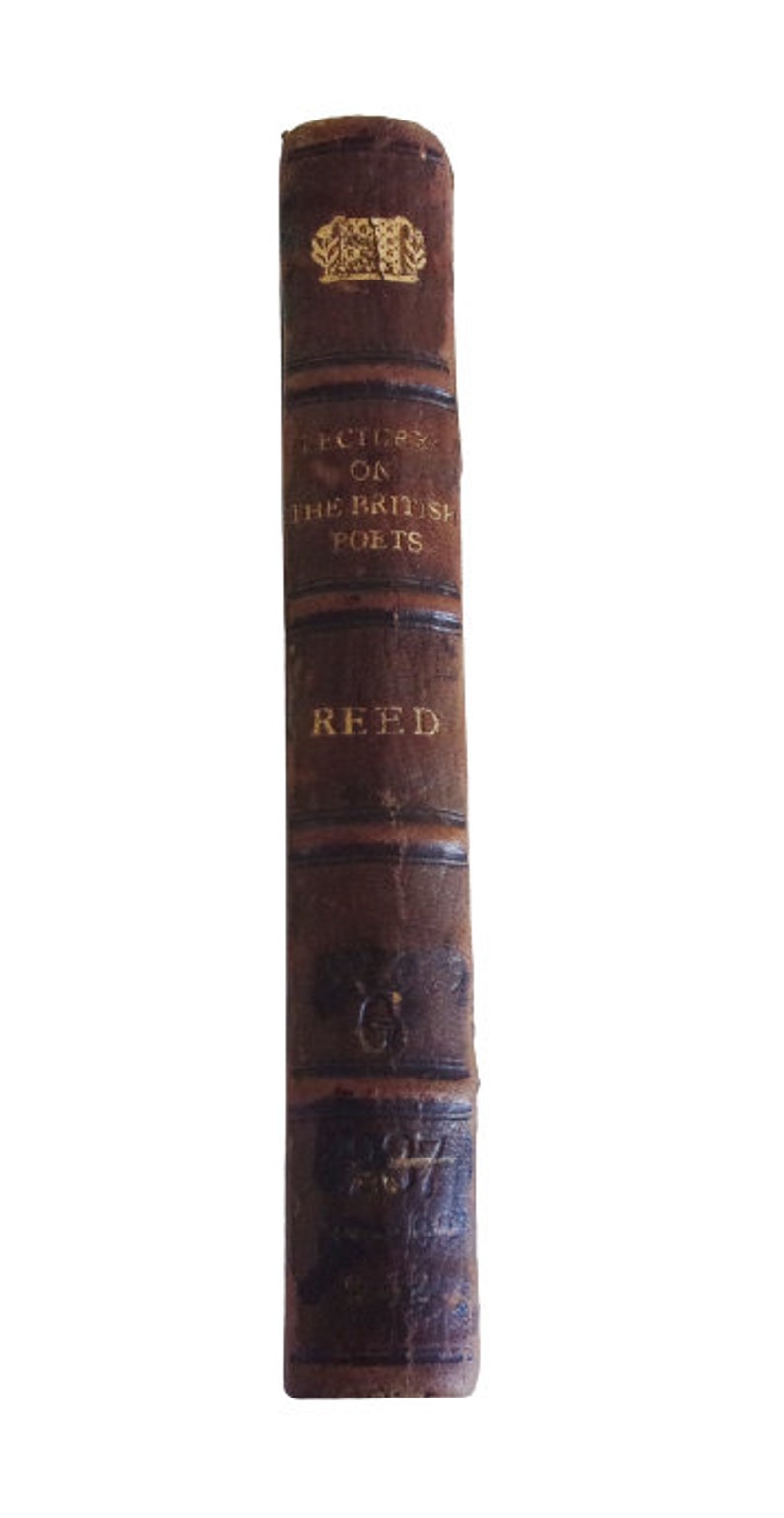 Puede incluir: Un libro encuadernado en cuero marr&oacute;n con letras doradas en el lomo. El t&iacute;tulo es "Lectures on the British Poets" de Reed.