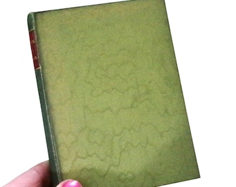 May include: A small, rectangular book with a textured, olive green cover. The spine is dark green with a red section. The book is held at an angle, with the cover facing the viewer.