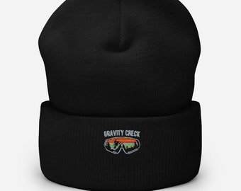 May include: Black beanie with a white embroidered design of a pair of ski goggles and the text "GRAVITY CHECK".