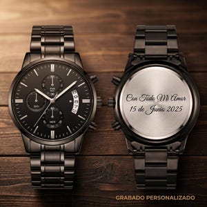 May include: Black stainless steel wristwatch with a round face and matching band. The watch face features multiple subdials and a date display. The back of the watch is engraved with text. The watch is displayed on a wooden surface.