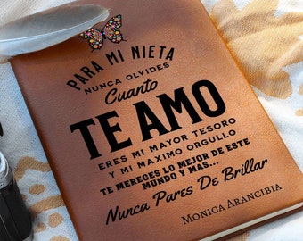 May include: A brown leather-bound journal with the text "PARA MI NIETA...TE AMO" in black. A colorful butterfly sticker is on the top left corner. A feather rests on the journal. The journal is on a patterned white surface.