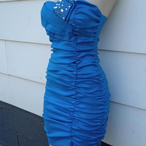 May include: A strapless blue dress with a ruched skirt and a jeweled embellishment on the bodice.