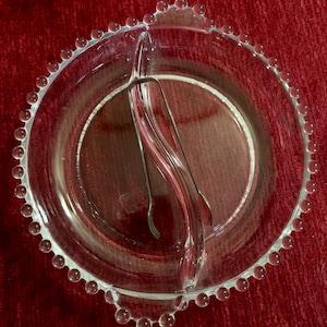 May include: A clear glass divided serving dish with a beaded rim. The dish has a built-in serving utensil.
