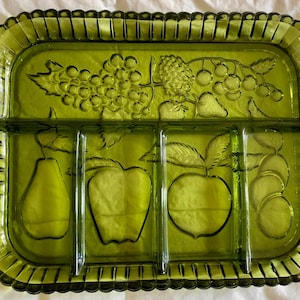 May include: A vintage green glass serving tray with a rectangular shape and a divided interior. The tray features embossed fruit designs, including grapes, apples, and pears. The edges have a decorative ribbed pattern and rounded handles.
