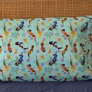 May include: A rectangular pillowcase with a light blue background featuring a repeating pattern of fairies in various poses, interspersed with purple and yellow floral designs. The fairies are depicted in different outfits.