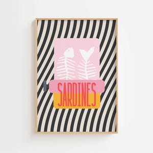 May include: A framed art print featuring a pink sardine can illustration with white fish bones. The word "SARDINES" is in orange and red text. The background has black and white diagonal stripes.