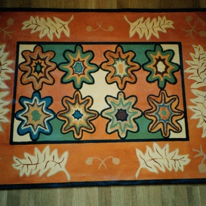 Può includere: Tappeto rettangolare con sfondo arancione e un motivo centrale di otto forme a stella in turchese, blu e verde. Il bordo presenta motivi di foglie e fiori color crema e arancione, con un bordo blu scuro.