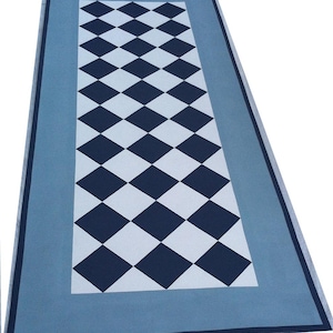 May include: A rectangular rug with a geometric diamond pattern. The central design features alternating navy blue and white diamonds. The rug is bordered by a light blue frame and a navy blue trim, creating a visually appealing contrast.