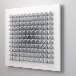 May include: A white wall with a gray and white geometric pattern made of squares. The squares are arranged in a grid pattern and are of varying sizes. The pattern is three-dimensional and creates a sense of depth.