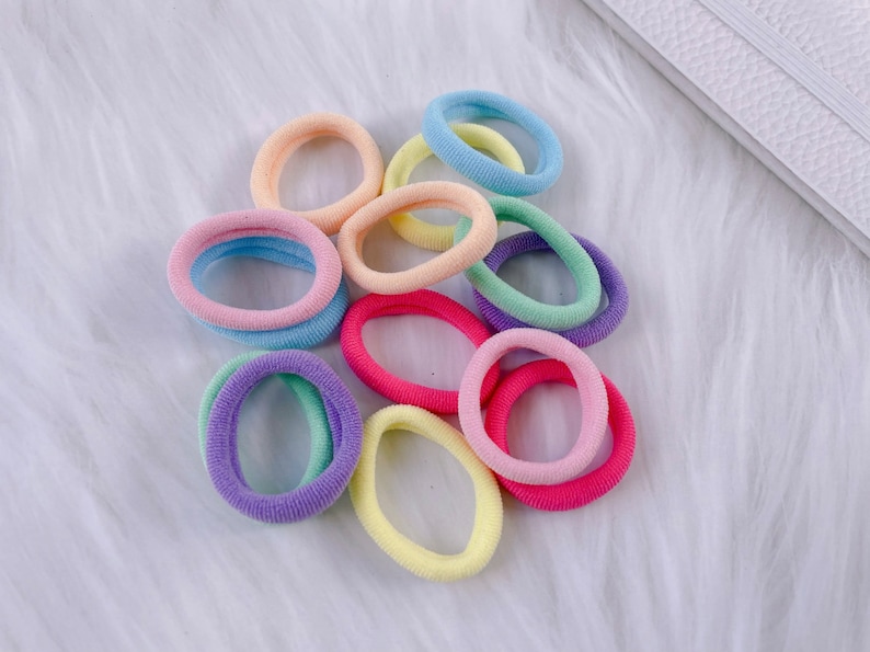 May include: A collection of colorful hair ties in pastel shades of pink, blue, yellow, and green. The hair ties are made of soft, stretchy fabric and are perfect for holding back hair.