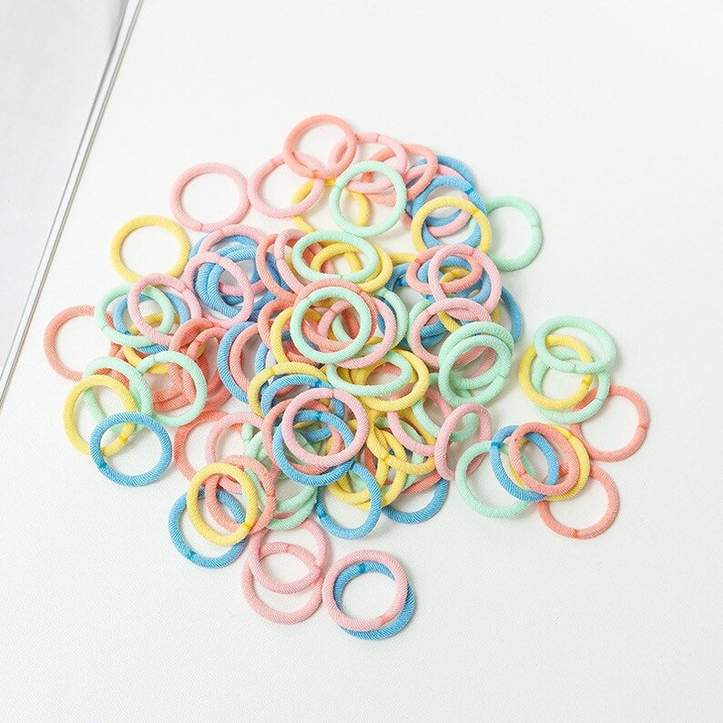 May include: A large pile of colorful hair ties in pastel pink, blue, and yellow.