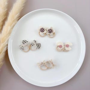 May include: A set of six hair ties with different fabric designs. The hair ties are white, brown, and black with floral and bow designs.