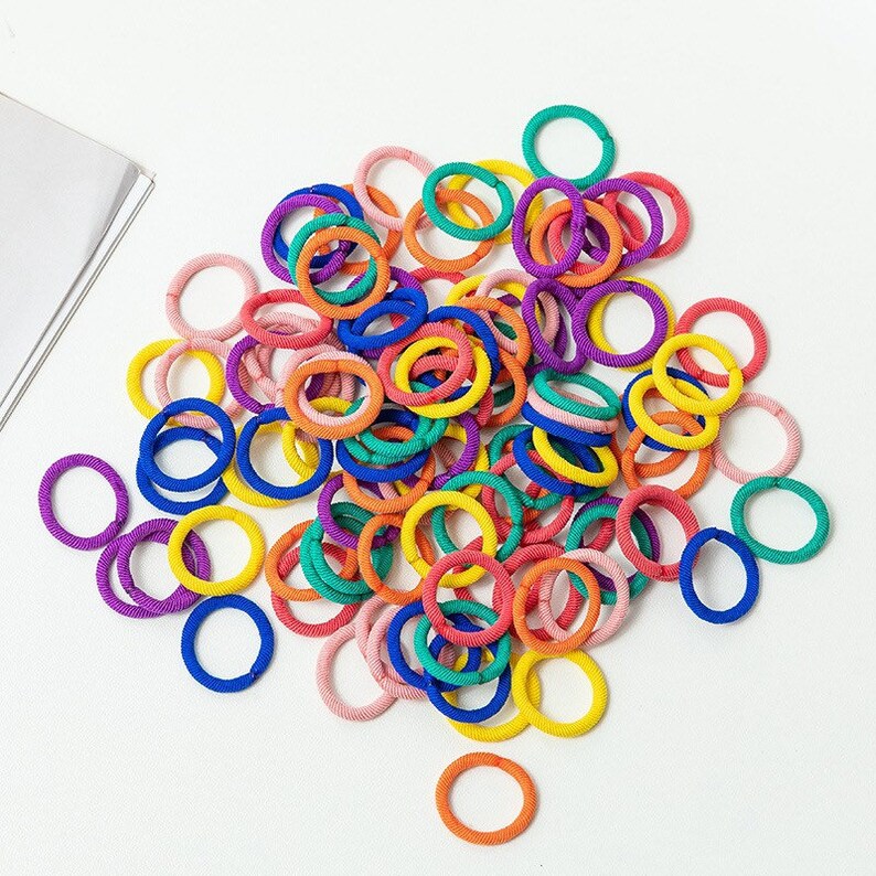 May include: A large pile of colorful hair elastics in a variety of colors, including pink, blue, green, yellow, and orange.