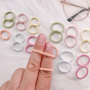 May include: A set of colorful fuzzy hair ties in various shades of pink, green, yellow, and blue. The hair ties are arranged in a circle on a white surface.