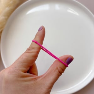 K&ouml;nnte beinhalten: Ein rosa Gummiband ist um zwei Finger gespannt.