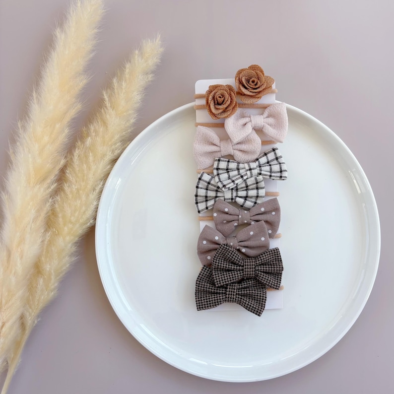 May include: Set of six hair bows in various patterns and colors, including brown, white, and black. The bows are arranged on a white card and include two brown felt flower bows.