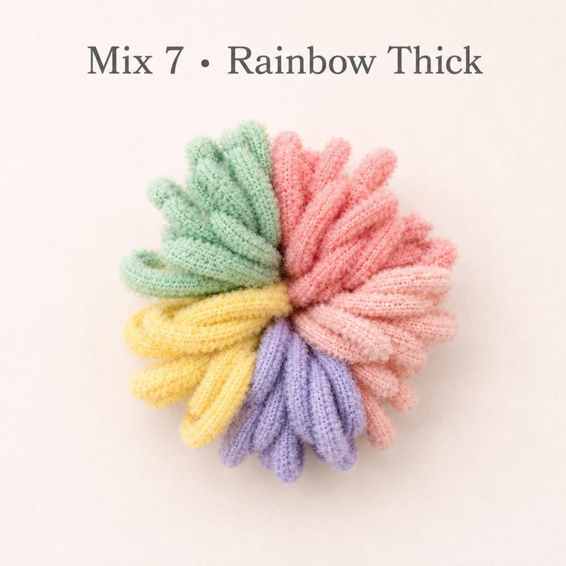 K&ouml;nnte beinhalten: Eine Ansammlung dicker Haargummis, die kreisf&ouml;rmig angeordnet sind, mit dem Text Mix 7 &bull; Rainbow Thick. Die Haargummis sind in Segmenten in Hellgr&uuml;n, zartem Rosa, Gelb und Hellviolett gehalten und haben eine strukturierte, strickartige Oberfl&auml;che.