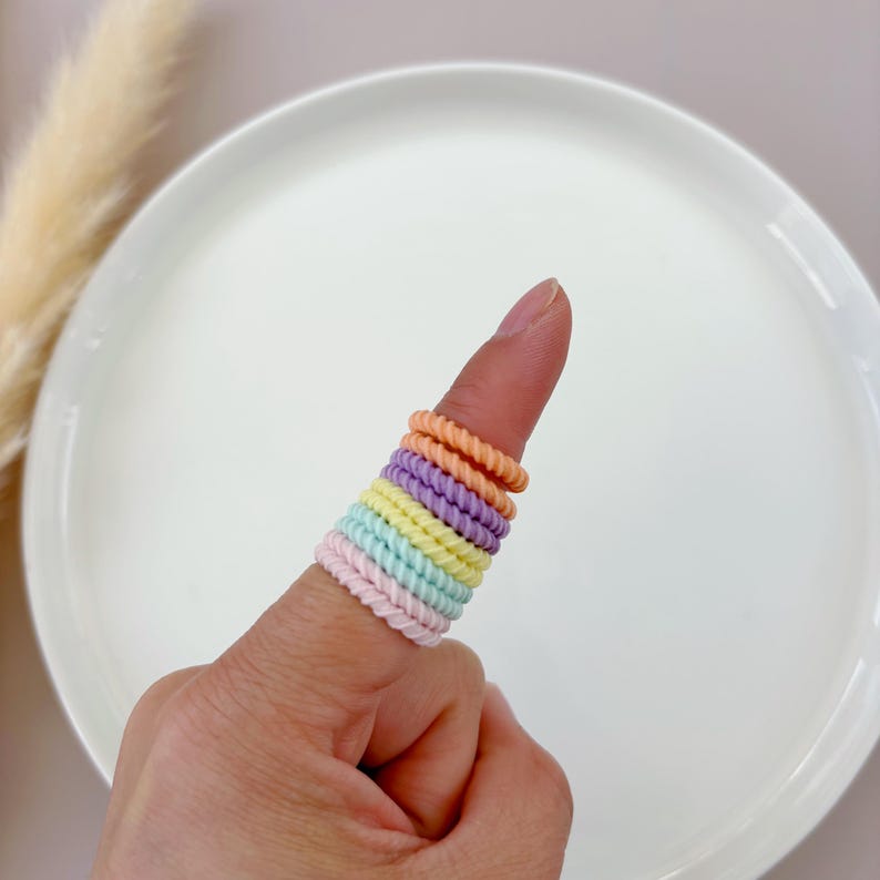Op de afbeelding: Een set kleurrijke haarbandjes in pasteltinten van paars, roze, geel en blauw. De haarbandjes zijn gemaakt van een zacht, rekbaar materiaal en perfect om haar vast te houden.