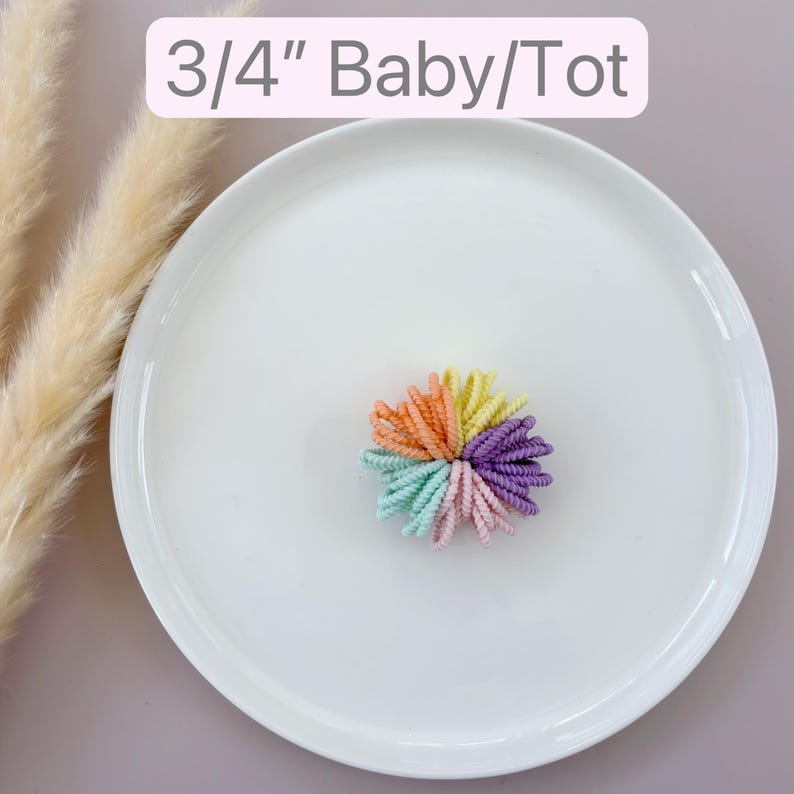 Op de afbeelding: Een set van 3/4 inch kleurrijke haarbandjes in een regenboogkleurenschema. De haarbandjes zijn in een cirkel op een wit bordje gerangschikt.
