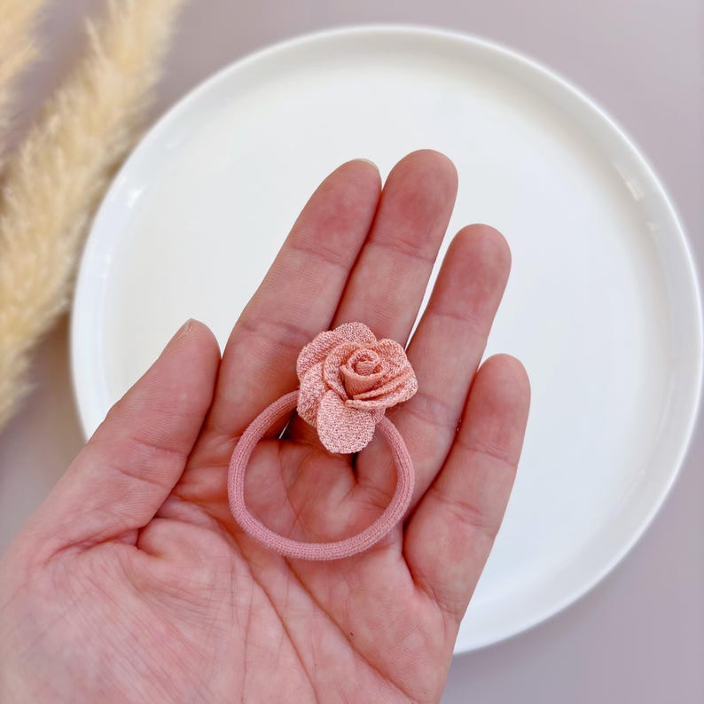 May include: A pink fabric rose hair tie. The hair tie is made of a soft, stretchy material and is perfect for holding back hair.
