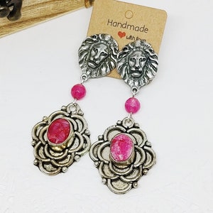 Peut inclure: Boucles d'oreilles en argent avec des accents de pierres roses et des breloques tête de lion. Les boucles d'oreilles sont faites à la main avec amour.