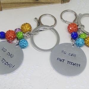 May include: Two silver keychains with a round charm that says "No day but today!" Each charm has a cluster of colorful rhinestone beads attached.