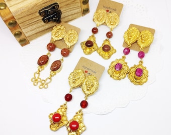 May include: Three pairs of gold lion head earrings with red and brown gemstone accents. The earrings are handmade and come on cards with the text "Handmade with love".