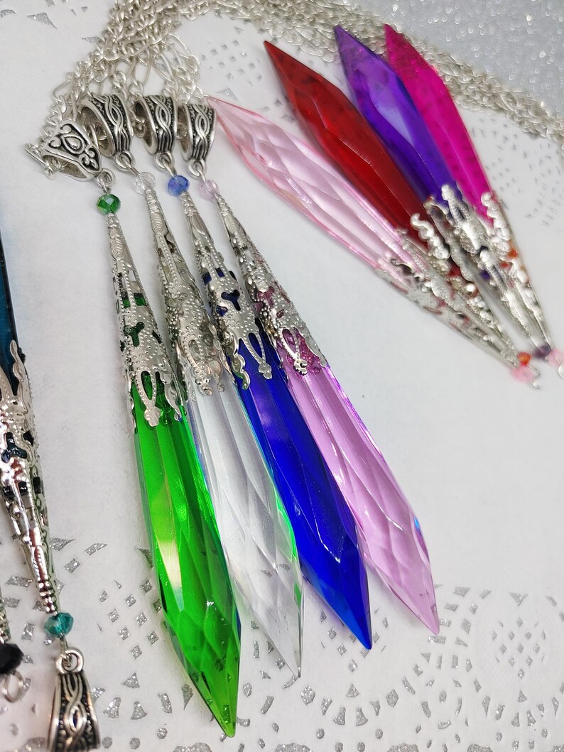 May include: A set of seven crystal pendants with silver-toned metal accents. The pendants are in various colors, including pink, red, purple, green, blue, and clear. The pendants are all shaped like a pointed teardrop.
