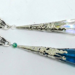 May include: Two silver necklaces with crystal pendants. The top pendant is clear and iridescent. The bottom pendant is a dark blue crystal.