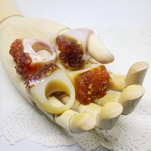 May include: Four resin rings with a white base and a brown, glittery top. The rings are displayed on a wooden hand.