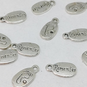 Può includere: Ciondoli in argento con la parola "Remember" e un design di impronta.