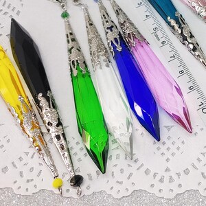 May include: Assortment of colorful crystal pendants with silver filigree accents. The pendants are approximately 7 inches long and feature a variety of colors, including yellow, black, green, blue, white, and pink.