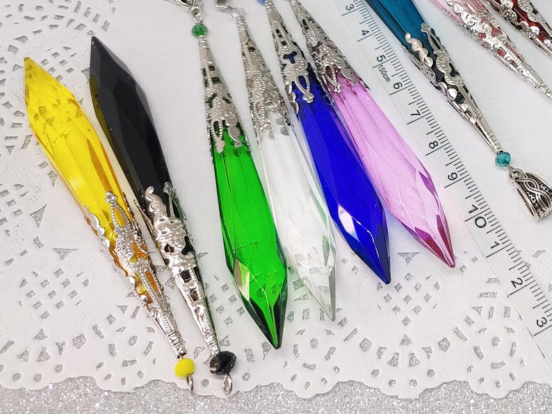 May include: Assortment of colorful crystal pendants with silver filigree accents. The pendants are approximately 7 inches long and feature a variety of colors, including yellow, black, green, blue, white, and pink.