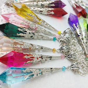May include: A collection of colorful crystal pendants with silver filigree accents. The crystals are in various shapes and sizes, including teardrop, point, and oval. The pendants are attached to silver chains.