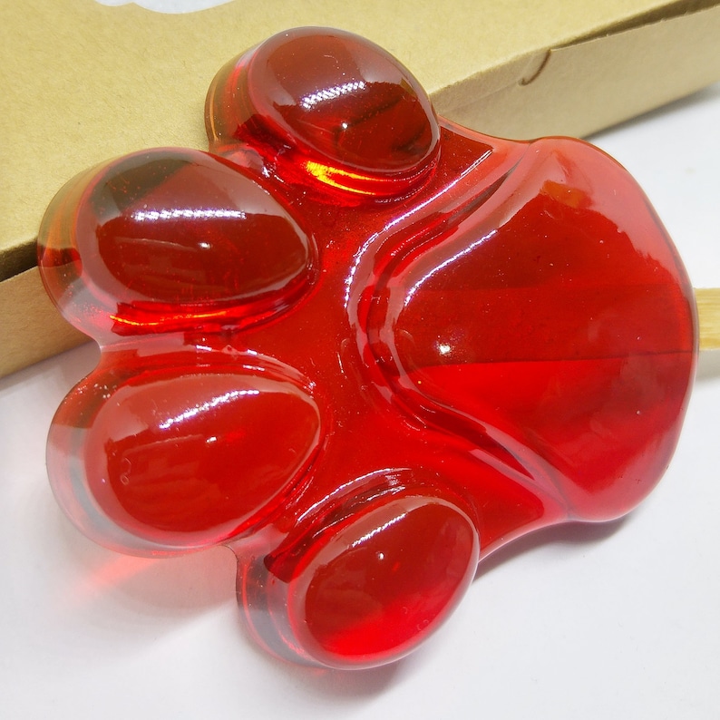 K&ouml;nnte beinhalten: Ein roter Lollipop in Form einer Pfote auf einem Stiel.