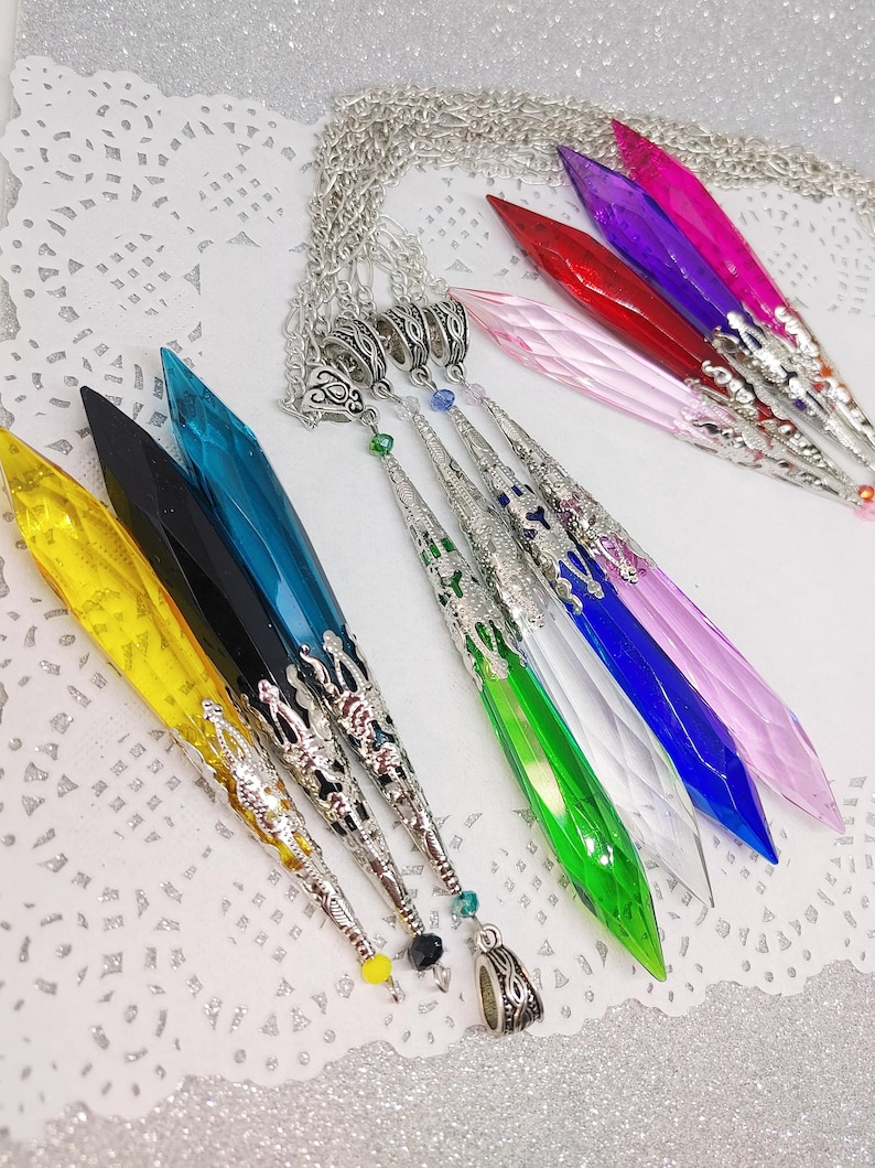 May include: A set of nine crystal point pendants with silver chain and ornate silver accents. The crystals are in various colors, including yellow, black, teal, green, clear, blue, pink, red, and purple.