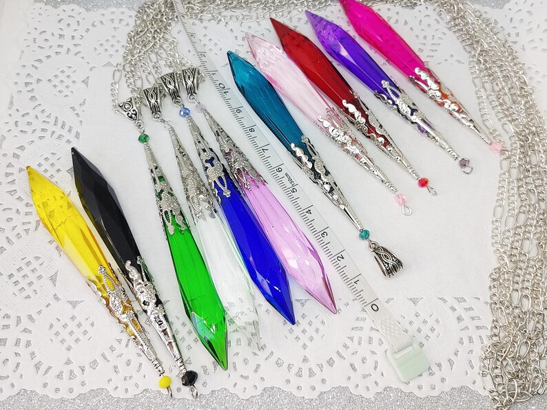 May include: A set of 10 crystal point pendants with silver-tone chain and ornate metal accents. The pendants are in various colors, including yellow, black, green, white, blue, pink, and purple.