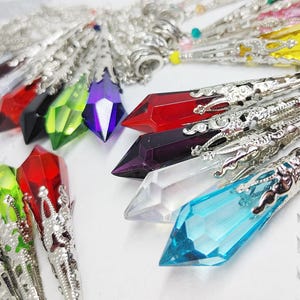 May include: A collection of colorful crystal pendants with silver filigree accents. The crystals are in various shapes and sizes, including teardrop, point, and oval. The pendants are strung on silver chains.