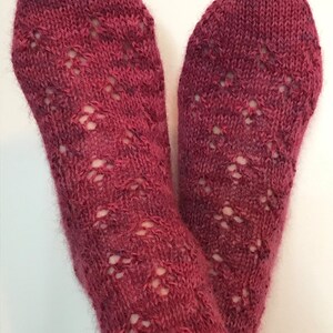 May include: A pair of red knitted socks with a lacy pattern. The socks are made with a soft yarn and have a delicate, feminine look.