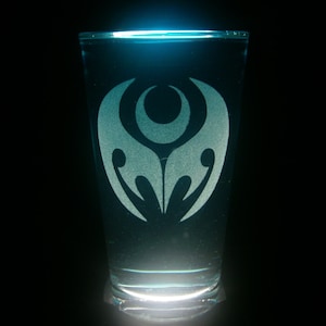 May include: A clear glass with a blue glow and a white etched design of a stylised symbol. The symbol is a circle with a crescent moon inside and two curved lines extending from the circle.